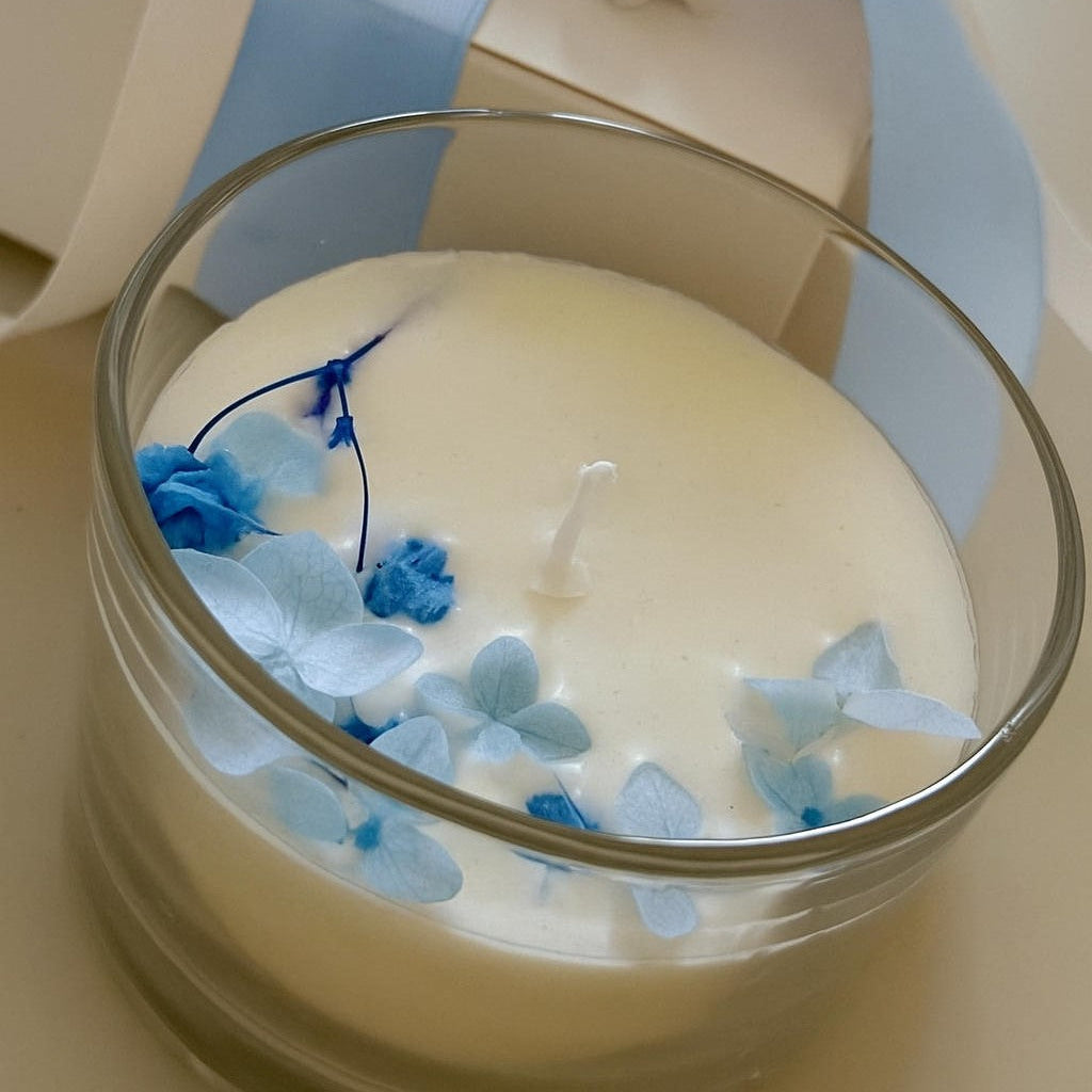 Candela artigianale decorativa in cera di soia, fiori essiccati azzurri e contenitore in vetro 